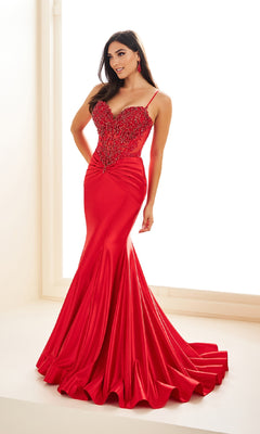 A woman wears the Ellie Wilde EW36004 Drop-Waist Mermaid Prom Dress: a fitted, floor-length red gown with thin straps, beaded detailing on a sheer corset bodice, and a flared hem.