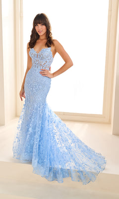 Woman wearing the Ellie Wilde EW36008 long embroidered prom dress poses indoors by a bright window, with one hand on her hip.