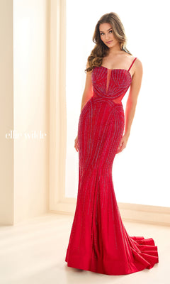 A woman in the Ellie Wilde EW36013 Long Beaded Prom Dress, a fitted floor-length red gown with thin straps and beaded details, stands by a window.
