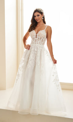 A woman stands indoors by a sunlit window wearing the Ellie Wilde EW36015, a sleeveless white long prom dress with a corset bodice, lace embroidery, floral appliqués, and a full tulle skirt.