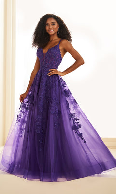 A woman smiles at the camera wearing the Ellie Wilde EW36015, a floor-length, sleeveless purple glitter tulle prom dress with lace embroidery and a sheer overlay.