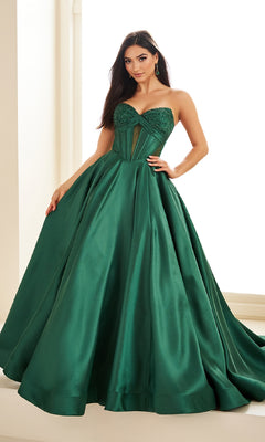 A woman poses indoors in the Ellie Wilde EW36025, a strapless, floor-length emerald green satin prom ball gown featuring a fitted, embellished corset bodice.