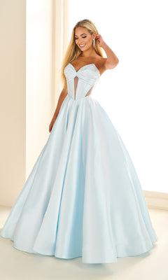 A woman wears the Ellie Wilde EW36025, a light blue satin long prom dress with a corset bodice and full skirt, standing indoors near a window.