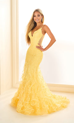 A woman smiles at the camera in a well-lit room, wearing the Ellie Wilde EW36041 long prom dress—a fitted, floor-length yellow gown with a v-neckline and lace detailing.