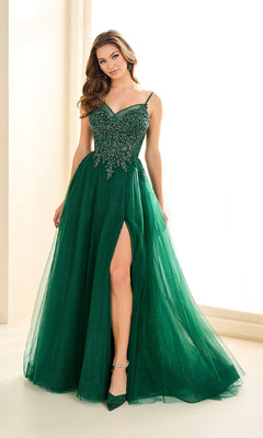A woman poses indoors in the Ellie Wilde EW36066, a sleeveless dark green ball gown with an embellished corset bodice and high slit, holding her skirt with one hand.