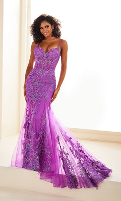 A woman poses against a light background in the Ellie Wilde EW36069, a fitted, floor-length purple prom dress with thin straps, floral embroidery, and a sheer corset bodice.