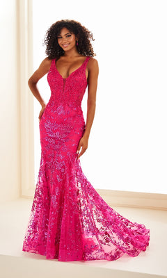 A woman in the Ellie Wilde EW36074 long prom dress, a fitted, floor-length bright pink mermaid gown with sequin embellishments, stands indoors smiling at the camera.