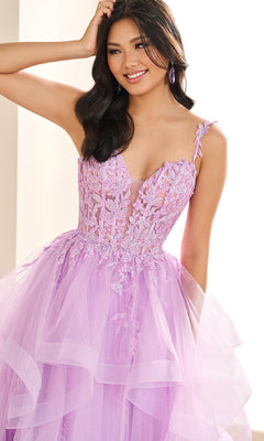 A woman smiles and raises a hand to her head while wearing the Ellie Wilde EW36081, a long lilac prom dress featuring floral embroidery and a layered glitter tulle skirt.