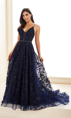 A woman is wearing the Ellie Wilde EW36088 long prom dress, featuring a deep navy blue color, thin straps, fitted bodice, and a flared embroidered tulle skirt with a small train.
