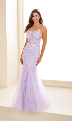 A woman stands indoors wearing the Ellie Wilde EW36090, a fitted lavender mermaid prom dress with floral lace appliques and thin straps.