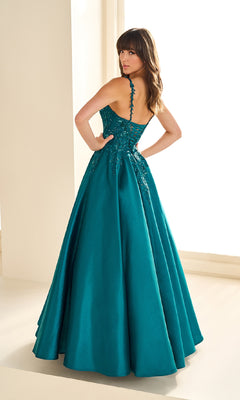 Woman wearing the Ellie Wilde EW36094 long prom dress in teal, featuring a corset bodice and lace detailing on brushed satin, standing indoors and looking over her shoulder.