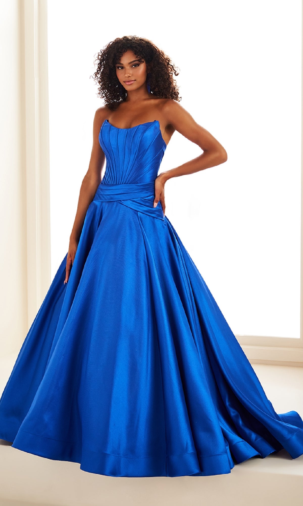 A woman wears the Ellie Wilde EW36105 long prom dress, a strapless mikado ball gown in royal blue with a fitted corset bodice and a full, floor-sweeping flared skirt.