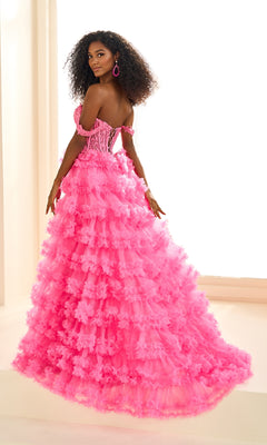 Woman wearing the Ellie Wilde EW36201 long prom dress—bright pink, off-the-shoulder with a ruffled skirt and lace applique corset bodice—posing indoors by a large window.
