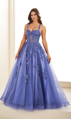 A woman wears the Ellie Wilde EW36202 long prom dress—a sleeveless purple ball gown with a corset bodice and floral appliqué—standing indoors against a light background.