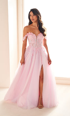 Woman wearing the Ellie Wilde EW36214 long prom dress—an off-the-shoulder, light pink a-line tulle gown with floral lace applique corset bodice and high slit—standing by a window indoors.