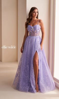 A woman in the Ellie Wilde EW36218 long prom dress—lavender, strapless, a-line with floral lace, 3D flowers, a sheer corset bodice, and high slit—stands indoors by a window.