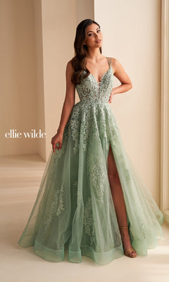 A woman wears the Ellie Wilde EW36226, a light green A-line prom dress with floral embroidery, corset bodice, and high slit. She stands indoors by a neutral wall, the gown's elegant silhouette highlighting her graceful presence.