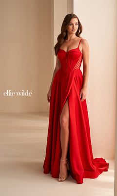 A woman stands indoors by a cream wall wearing the Ellie Wilde EW36227, a red, floor-length satin prom dress featuring an a-line silhouette, thigh-high slit, spaghetti straps, and open back.