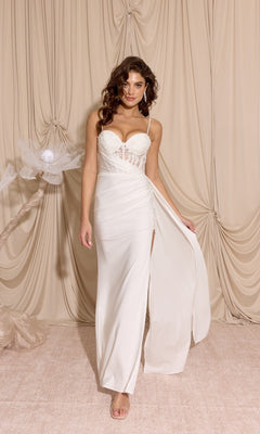A woman in the Eureka EK166 long white prom dress, featuring a sleeveless design, sheer-embroidered bodice, and high slit, stands against a beige draped fabric backdrop.