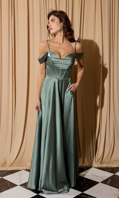 A woman models the Eureka EK176 long prom dress in sage green satin with cold shoulder and spaghetti straps, standing before beige curtains on a black-and-white tiled floor.