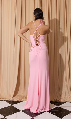 Wearing the Eureka EK186 Long Prom Dress in light pink, featuring a corset bodice and crisscross lace-up back, a person stands on black and white tile flooring before beige curtains.