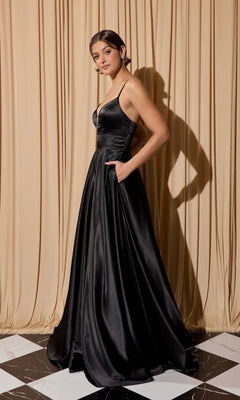 A woman wearing the Eureka EK190 long prom dress, a sleeveless black satin gown with pockets and an A-line skirt, stands on a black and white tiled floor in front of beige curtains.