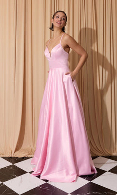 A woman stands on a black-and-white tiled floor, wearing the pink Eureka EK190 long prom dress with thin straps, open back, and pockets, posed in front of beige draped curtains.