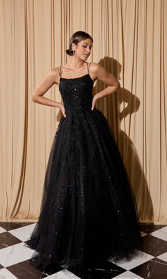 A woman stands on a black-and-white tiled floor before beige curtains, wearing the Eureka EK197 long black prom dress—sleeveless, with thin straps and shimmering sequin details.