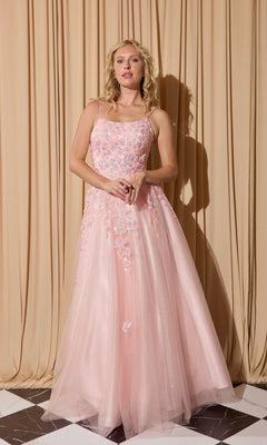 A woman stands before beige curtains wearing the Eureka EK197 long prom dress, a floor-length, light pink glitter tulle gown with delicate floral embroidery and thin straps.