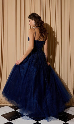 A woman wearing the Eureka EK197 long prom dress in dark blue glitter tulle stands on a black-and-white tiled floor, facing away, with beige curtains behind her.