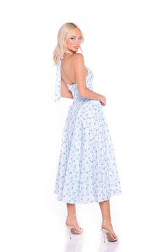 A woman models the Light Blue Floral Halter Summer Midi Dress: Eliza, standing in high heels and facing slightly backward against a white background.