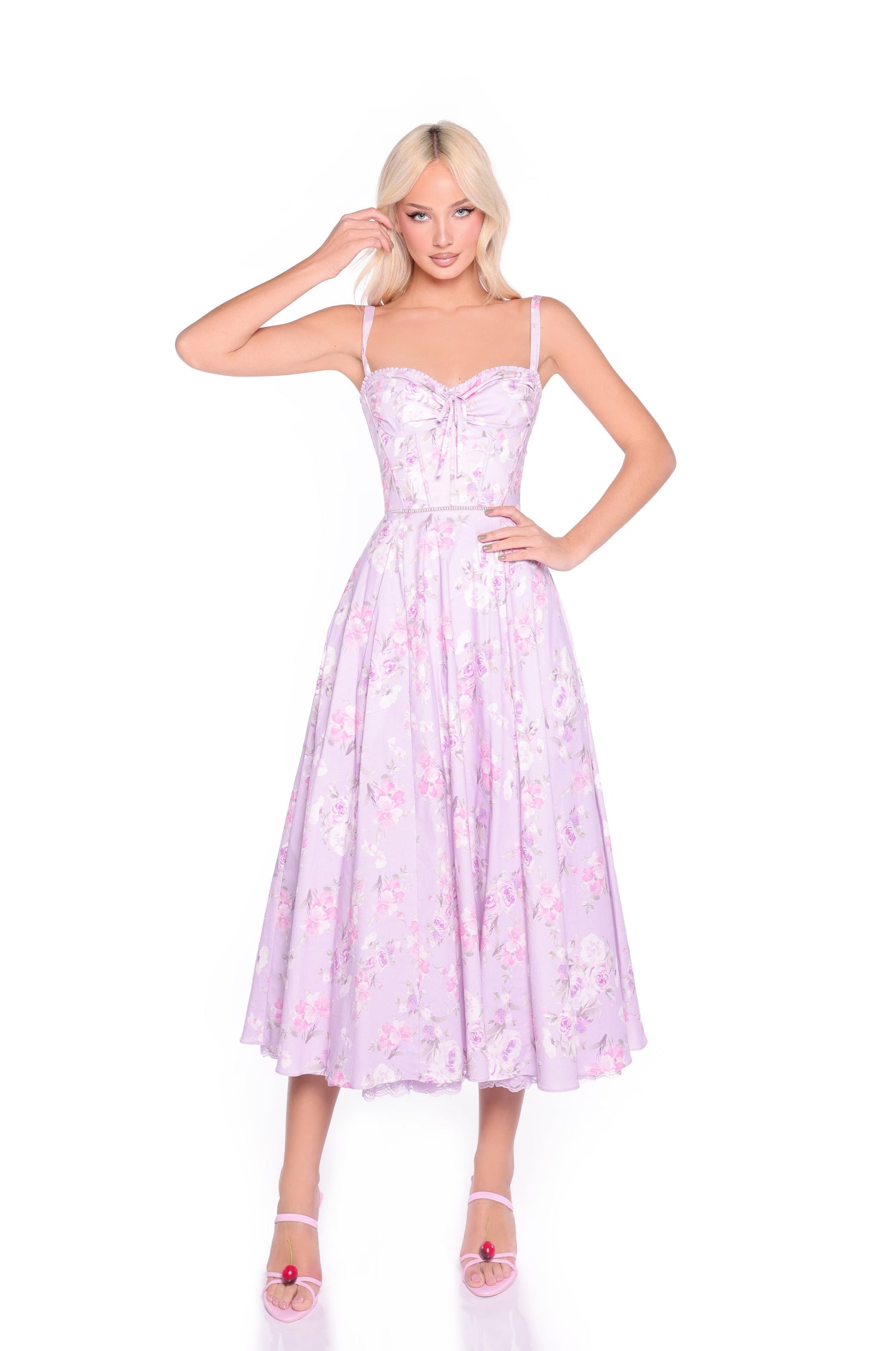 A woman in the Lilac Floral Print Midi Summer Dress: Elle, featuring a corset bodice and spaghetti straps, stands against a white background wearing pink heels.