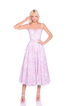 A woman in the Lilac Floral Print Midi Summer Dress: Elle, featuring a corset bodice and spaghetti straps, stands against a white background wearing pink heels.