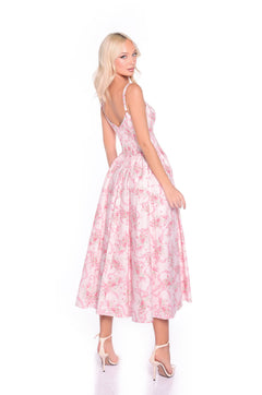Woman wears the Emilia blush pink print casual midi dress with a corset bodice and spaghetti straps, standing in white high heels and looking over her shoulder against a plain white background.