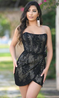 Woman wearing the Everly Strapless Ivory Lace Graduation Party Dress, featuring a chic wrap-style skirt—a stylish update on the classic strapless graduation dress—standing outdoors with greenery in the background.