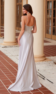 A woman models the Nox Anabel F1570, a silver beaded-corset long prom dress with thin straps, standing on a tiled patio before tall windows and columns.