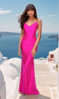 A woman in a vibrant pink La Femme Backless Long V-Neck Prom Dress 28287 stands on stone steps, her striking gown contrasting with the white buildings and blue sea behind her.