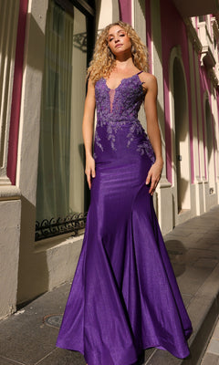 A woman with curly blonde hair wears the Lace-Up Embroidered Bodice Long Prom Dress G1364, a floor-length mermaid gown with floral lace details in purple, as she stands outside a pink and cream building.