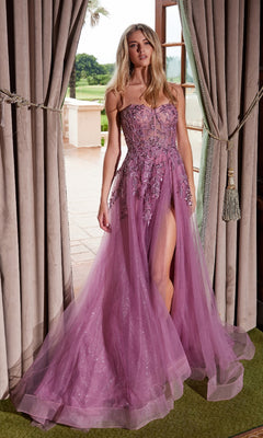 A woman in the Nox Anabel G1371 strapless long prom ball gown, featuring glitter, floral embellishments, and a thigh-high slit, stands before open curtains.
