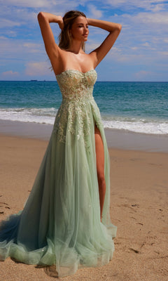 A woman in the Nox Anabel G1371 Strapless Long Prom Ball Gown with embroidered lace and a thigh-high slit stands on a sandy beach by the ocean under a partly cloudy sky.