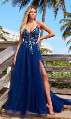A woman in the Nox Anabel G1649 Lace-Up Long A-Line Prom Dress with a v-neck, floral embellishments, and thigh-high slit stands by a wooden railing beneath palm trees.