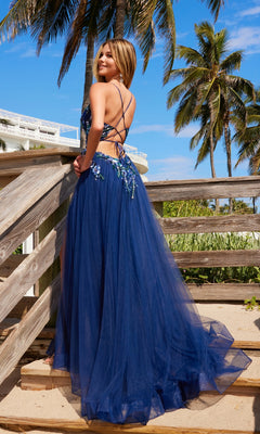 A woman wearing the Nox Anabel G1649 Lace-Up Long A-Line Prom Dress stands on wooden steps by palm trees and a sunny beach.