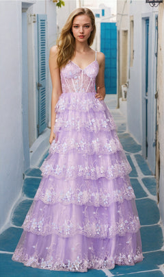 A woman stands on a stone path in an outdoor setting, wearing the Long Ruffled A-Line Prom Ball Gown: Juliet JT2454K, featuring floral lace details. White buildings with blue shutters appear in the background.