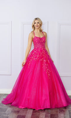 A woman poses indoors against a light-colored, paneled wall wearing the Glitter-Tulle Long Prom Ball Gown H1271, featuring bright pink glitter tulle, floral embellishments, and thin straps.