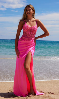 A woman in the Sheer-Bodice Long Prom Dress: Nox Anabel H1670, a bright pink beaded gown with a high slit, stands on a sandy beach with the ocean and sky in the background.