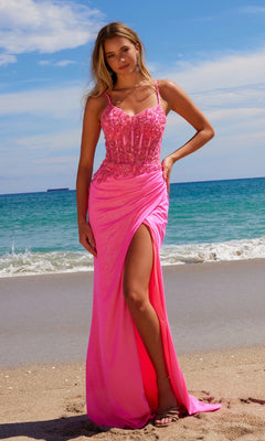 A woman in the Sheer-Bodice Long Prom Dress: Nox Anabel H1670, featuring bright pink beading and a thigh-high slit, stands on a sandy beach near the ocean under a partly cloudy sky.