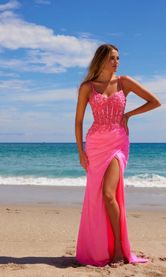 Wearing the Sheer-Bodice Long Prom Dress: Nox Anabel H1670, a woman stands on a sandy beach in a bright pink sequined gown with a thigh-high slit, framed by the ocean and blue sky.