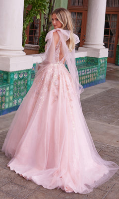 A woman in the Nox Anabel H1680 Shoulder-Bows Long Prom Dress—a light pink, floor-length, backless gown with tulle and sequins—stands outdoors near tiled walls and pillars, gazing over her shoulder.