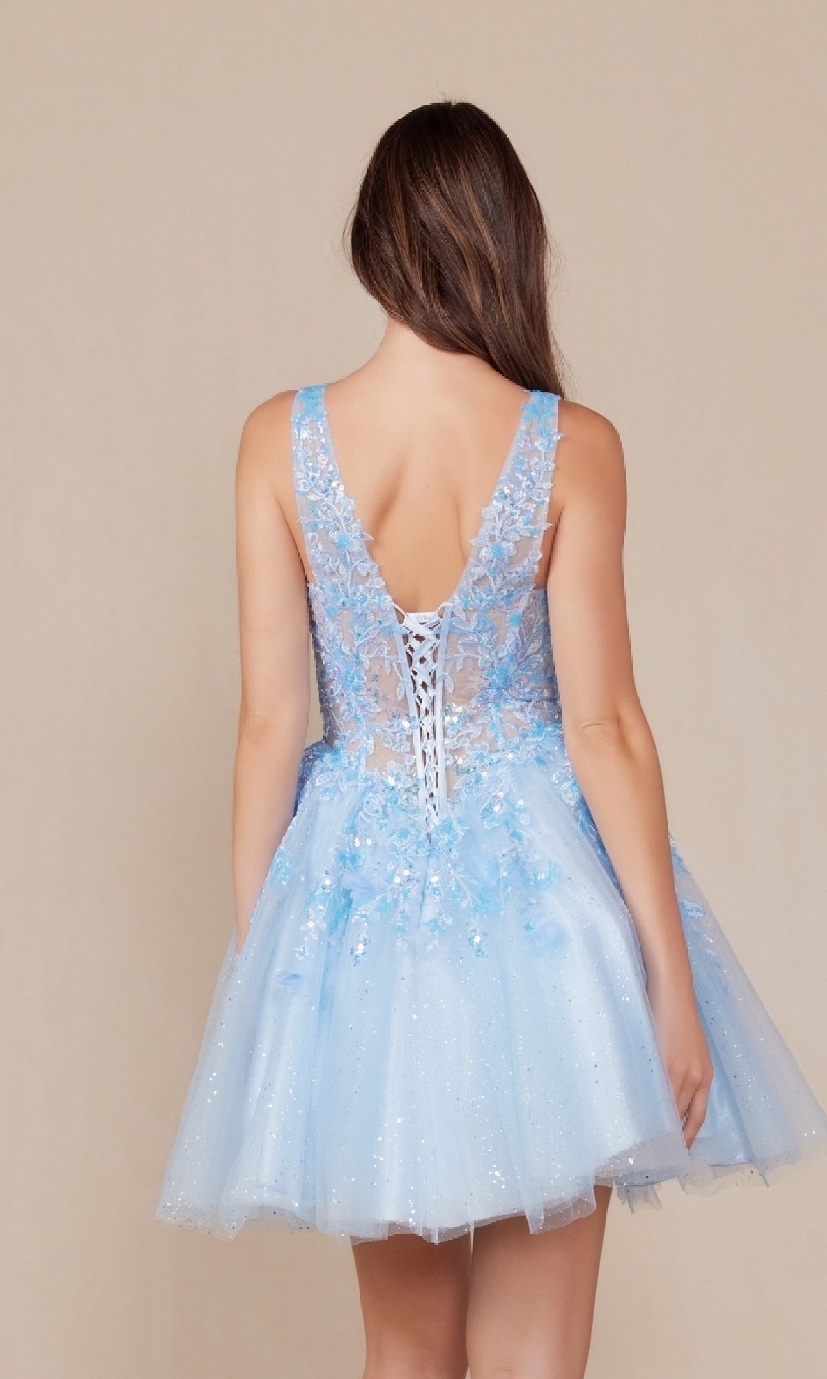 A woman with long brown hair is shown from behind wearing the Embroidered-Bodice Short A-Line Hoco Dress H846, a sleeveless light blue babydoll party dress with a lace-up back, floral appliqué, and an embroidered-lace sweetheart bodice.