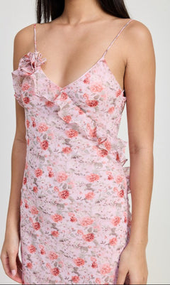 A woman wearing the Pink Floral Backless Summer Maxi Dress with ruffle details and spaghetti straps stands against a plain background.